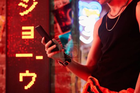 Photo for Hand of young man wearing black singlet, bracelet and neck chain against wall with hieroglyph meaning best ramen in cyberpunk bar or cafe - Royalty Free Image