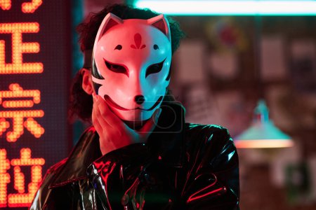 Photo for Young woman in fox mask standing against hieroglyph meaning best ramen while spending time in night club, cyberpunk bar or cafe - Royalty Free Image