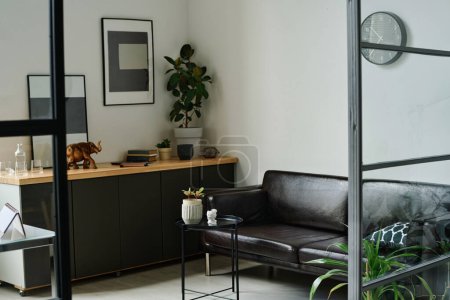 Photo for Corner of spacious hi-tech office with comfortable black leather couch standing in front of small round decorative table with flowerpot - Royalty Free Image