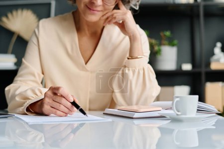 Téléchargez les photos : Main de femme comptable mature pointant vers un document financier ou un contrat d'affaires tout en lisant ses points et en vérifiant les informations - en image libre de droit