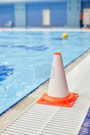 Foto de Cono plástico blanco y naranja de pie junto a la piscina con agua azul puro preparado para la natación o el juego deportivo profesional - Imagen libre de derechos
