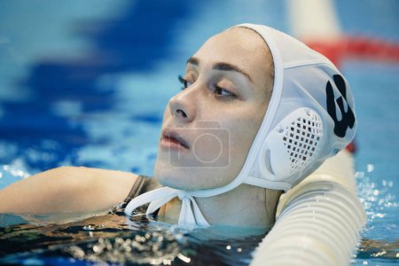 Photo for Young restful female water polo player in swimming cap standing in deep water of pool by finish line and having break between trainings - Royalty Free Image