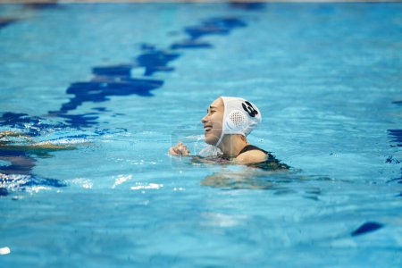 Foto de Joven deportista alegre en ropa deportiva nadando en piscina profunda con agua azul pura mientras juega waterpolo durante el entrenamiento o el juego - Imagen libre de derechos