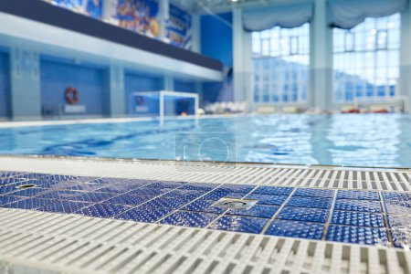 Foto de Enfoque en el suelo húmedo de la piscina azul con rejilla de plástico blanco contra la piscina ancha y profunda con agua pura transparente en el centro deportivo - Imagen libre de derechos