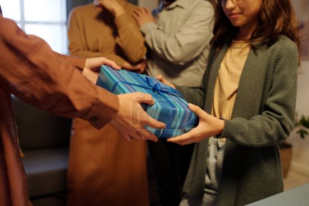 Téléchargez les photos : Plan recadré d'une jeune fille recevant Hanoukka présente dans une boîte cadeau enveloppée de papier rayé bleu de sa mère - en image libre de droit