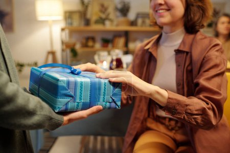 Téléchargez les photos : Gros plan de la jeune femme heureuse gardant les mains sur le dessus de la boîte-cadeau emballée enveloppée dans du papier bleu tout en passant Hanoukka cadeau à sa fille - en image libre de droit
