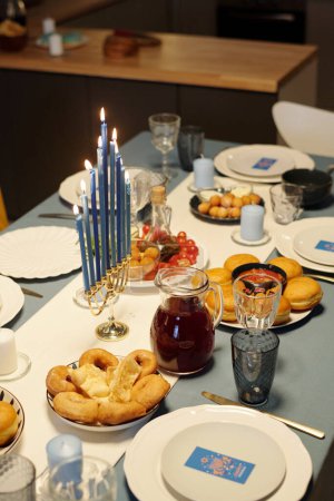 Foto de Mesa servida con nueve velas menorah rama rodeada de golosinas caseras para los miembros de la familia judía e invitados - Imagen libre de derechos