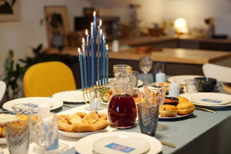 Photo for Traditional Hanukkah menorah with nine blue burning candles standing in the center of served table with homemade food and drinks - Royalty Free Image