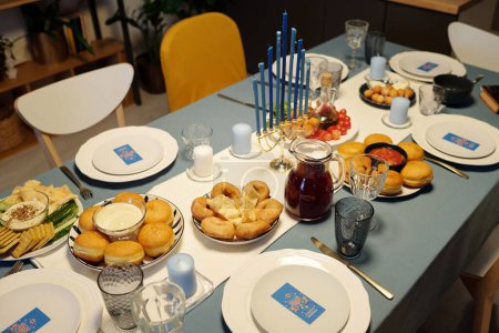 Photo for Table served with traditional Hanukkah food and drinks, menorah candlestick, glassware and plates with greeting cards - Royalty Free Image