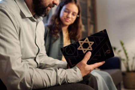 Photo for Focus on Torah with star of David on black cover in hands of bearded man sitting next to his daughter and reading Scripture text - Royalty Free Image