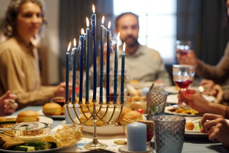Téléchargez les photos : Brûler des bougies sur le chandelier menorah debout sur la table servi avec de la nourriture et des boissons maison pendant la célébration de Hanoukka - en image libre de droit