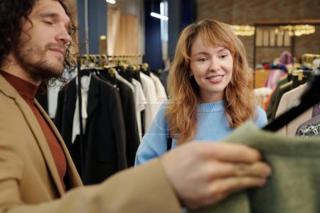 Téléchargez les photos : Jeune couple regardant à travers la nouvelle collection saisonnière de vêtements en boutique pendant les achats tout en choisissant quelque chose à acheter - en image libre de droit