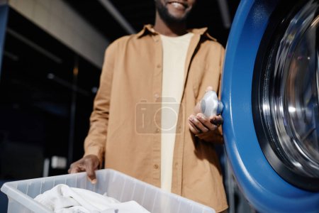 Téléchargez les photos : Coupé coup de gars afro-américain tenant bouton sur la porte ronde de la machine à laver automatique avant de mettre là ses vêtements - en image libre de droit