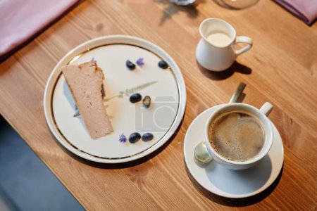 Photo for Above angle of wooden table in restaurant or cafe with cup of aromatic cappuccino and plate with piece of fresh tasty cheesecake - Royalty Free Image