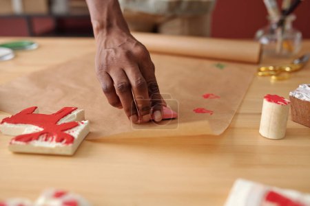 Foto de Mano de chica afroamericana creativa haciendo impresiones en papel con una pequeña pieza de trabajo con pintura roja mientras se prepara para la Navidad - Imagen libre de derechos