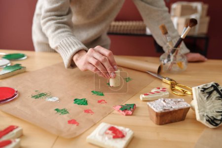 Foto de Mano de mujer joven irreconocible haciendo impresiones de símbolos navideños en papel mientras se inclina sobre la mesa con varios suministros - Imagen libre de derechos