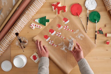 Téléchargez les photos : Mains de jeune femme méconnaissable imprimant une pièce de cerf sur du papier avec d'autres symboles de Noël imprimés tout en restant près de la table - en image libre de droit