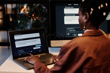 Téléchargez les photos : Écran d'ordinateur portable avec tâche génératrice d'IA et vue arrière de la jeune créatrice afro-américaine appuyant sur les touches du clavier - en image libre de droit