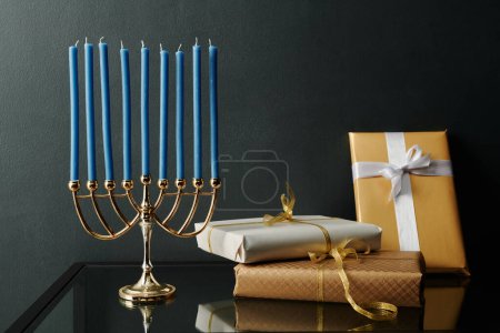 Foto de Nueve velas azules menorah de pie sobre la mesa junto a un montón de regalos preparados para celebrar Hanukkah - Imagen libre de derechos