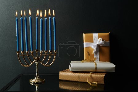 Foto de Menorah con nueve velas azules ardiendo de pie en la mesa junto a la pila de regalos preparados para la celebración de Hanukkah - Imagen libre de derechos