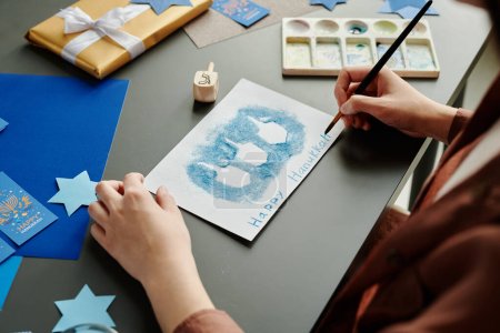 Téléchargez les photos : Mains de jeune femme créative avec pinceau sur la nouvelle carte postale Hanoukka avant la célébration des fêtes juives - en image libre de droit