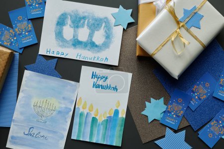 Téléchargez les photos : Au-dessus de l'angle de la variété des cartes postales faites à la main et des symboles de Hanoukka couché sur la table à côté de la pile de boîtes-cadeaux enveloppées dans du papier brillant - en image libre de droit