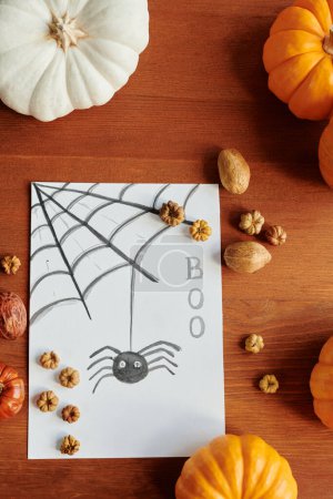 Photo for Above shot of handmade Halloween greeting card lying on wooden table among group of pumpkins, several walnuts and tiny decorations - Royalty Free Image