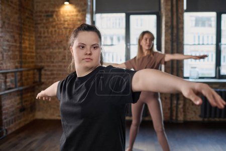 Photo for Young active woman with Down syndrome in black t-shirt outstretching arms during physical exercise while standing in front of camera - Royalty Free Image