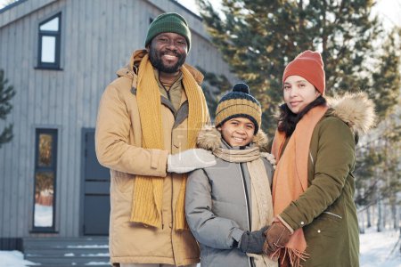 Téléchargez les photos : Joyeux jeune interculturel mère et père en vêtements d'hiver chauds entourant leur fils mignon heureux tout en profitant des vacances d'hiver - en image libre de droit