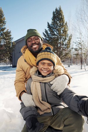 Photo for Happy young African American man and his cute son in warm winterwear taking selfie and looking at camera on winter weekend - Royalty Free Image