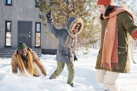 Photo for Cute laughing African American boy in winterwear playing with his mother and father in snowdrift while enjoying winter vacation - Royalty Free Image