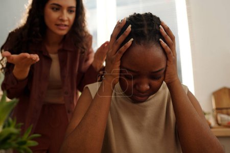 Foto de Enojada joven afroamericana que mantiene la cabeza en las manos mientras su novia nerviosa grita durante la discusión - Imagen libre de derechos