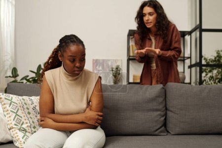 Photo for Offended African American girl sitting on couch against her irritated girlfriend trying to explain something during quarrel - Royalty Free Image