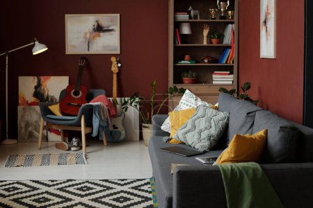 Photo for Grey comfortable couch with group of soft cushions standing along wall with abstract painting against armchair with acoustic guitar - Royalty Free Image