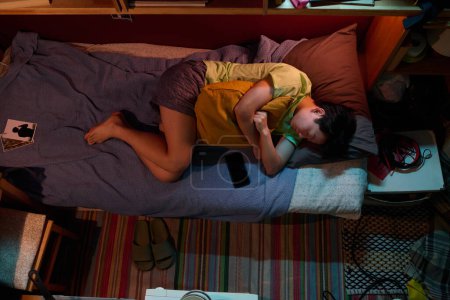Foto de Sobre el ángulo de la joven mujer asiática con almohada que duerme en una cama individual en un pequeño apartamento o microplano con variedad de cosas - Imagen libre de derechos