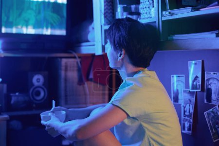Téléchargez les photos : Jeune femme asiatique avec bol vide et baguettes assis devant un vieux téléviseur et regarder un film ou diffuser après le déjeuner à la maison - en image libre de droit