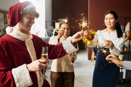 Photo for Young cheerful office managers with burning sparklers and flutes of champagne enjoying Christmas party after working day - Royalty Free Image