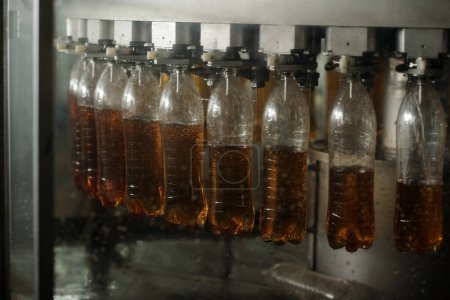 Photo for Row of several transparent plastic bottles hanging on belt conveyor during process of pouring soda or lemonade before packaging - Royalty Free Image