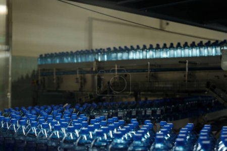 Téléchargez les photos : Abondance de bouteilles en plastique bouchées avec de l'eau minérale purifiée se déplaçant sur bande transporteuse dans une grande usine moderne de boissons en bouteille - en image libre de droit