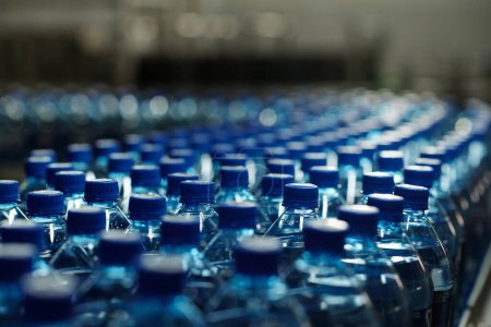 Téléchargez les photos : Bouteilles en plastique emballées avec bouchons bleus contenant de l'eau minérale purifiée se déplaçant sur la ligne de production devant la caméra à l'usine - en image libre de droit