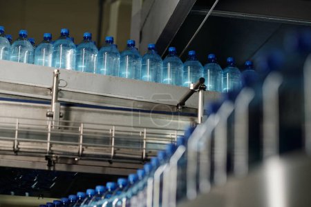 Téléchargez les photos : Rangée de bouteilles en plastique bouchées avec de l'eau minérale plate et gazeuse se déplaçant sur une énorme chaîne de montage à l'usine de boissons en bouteille - en image libre de droit