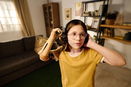 Photo for Youthful amputee girl doing dance moves to music in headphones in the center of spacious living room while enjoying leisure - Royalty Free Image