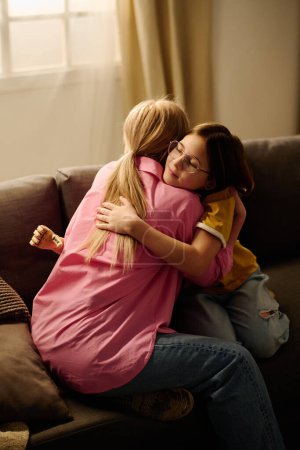 Photo for Young affectionate single mother giving hug to her cute pre-teen daughter with partial arm while both sitting on couch in living room - Royalty Free Image