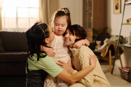 Foto de Linda niña con síndrome de Down abrazando a dos mujeres felices en ropa de casualwear mientras que uno de ellos mirando a su adorable hija - Imagen libre de derechos
