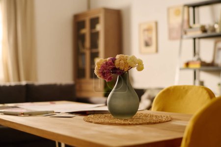 Téléchargez les photos : Table avec bouquet de fleurs dans un vase gris et deux chaises jaunes se tenant à proximité dans le centre du salon de l'appartement moderne - en image libre de droit