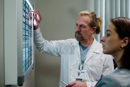 Foto de Médico maduro en bata de laboratorio y su asistente mirando la gammagrafía cerebral y los resultados de aprendizaje del examen médico del paciente con enfermedad - Imagen libre de derechos