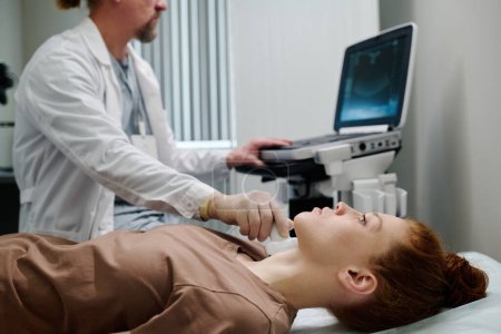 Téléchargez les photos : Jeune patiente allongée devant une caméra dans un cabinet médical lors de diagnostics par échographie effectués par un endocrinologue - en image libre de droit
