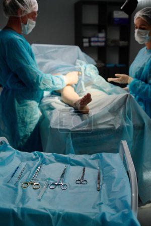 Foto de Herramientas operativas en servilleta azul y cirujano con asistente femenino en exfoliantes médicos, guantes y máscaras que rodean al paciente - Imagen libre de derechos