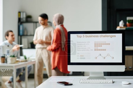 Photo for Screen of desktop computer with graphic data standing on desk against group of modern Muslim brokers having meeting in office - Royalty Free Image