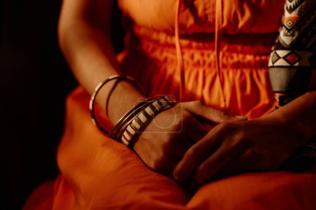 Téléchargez les photos : Gros plan d'une femme méconnaissable en tenue dopaminergique, bandeau ethnique et bracelets assis devant la caméra en studio - en image libre de droit